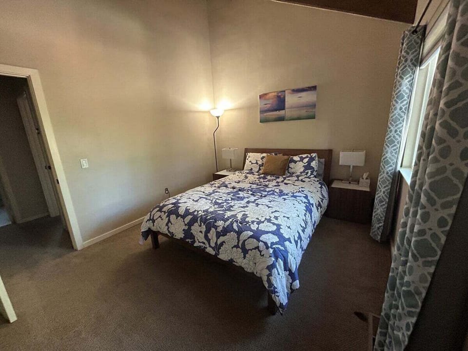 Upstairs queen bedroom with queen bed, nightstands, lamps, floor lamp, window, curtains, wall art, doorway, and hallway view.
