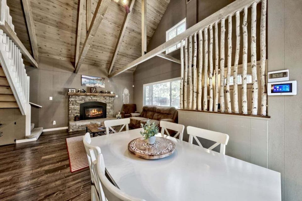 Dining area with seating, fireplace, sofa, armchair, coffee table, large window, stairway, and vaulted ceiling.