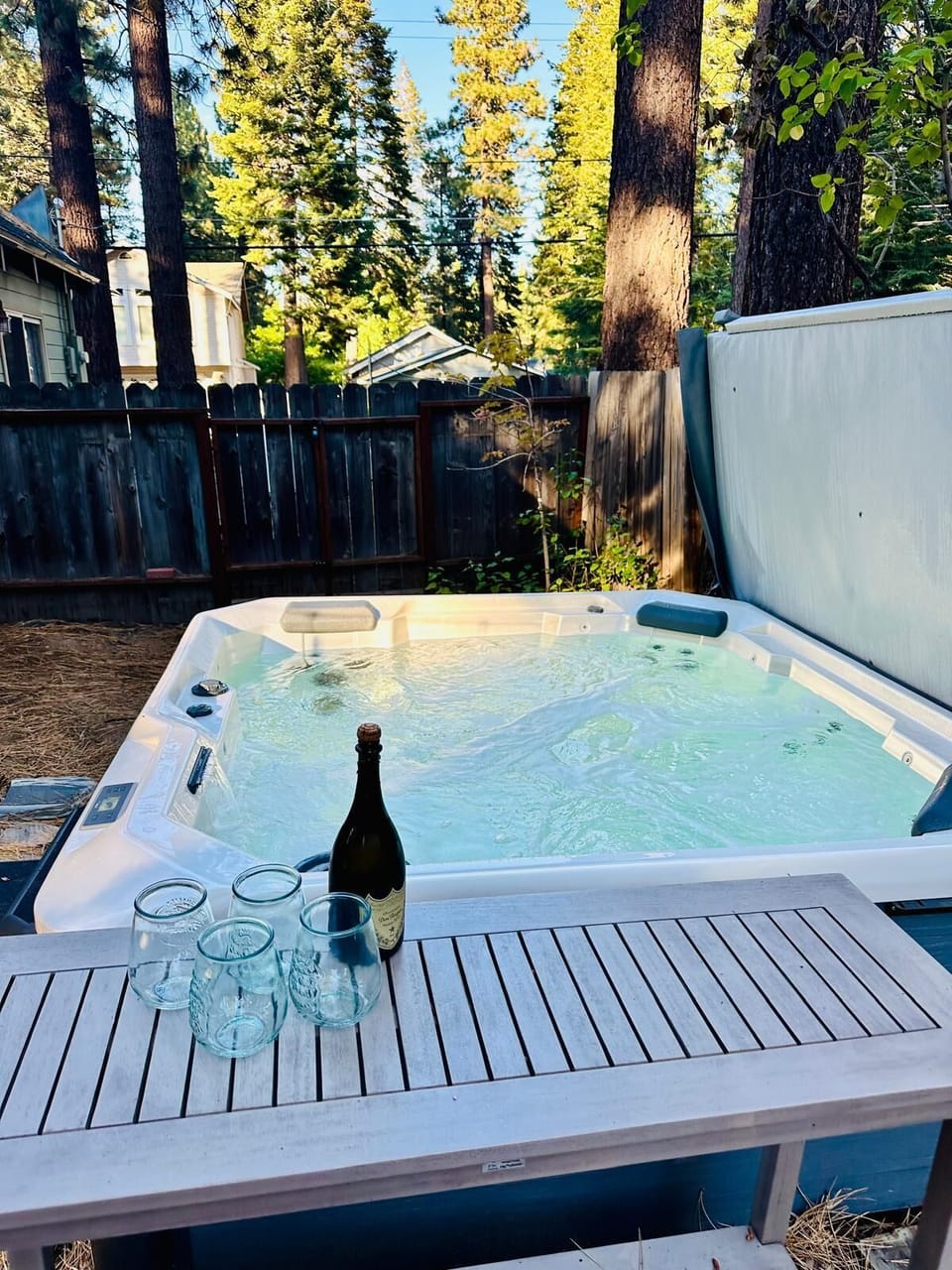 Hot tub area with bench, fence, trees, and water in view.