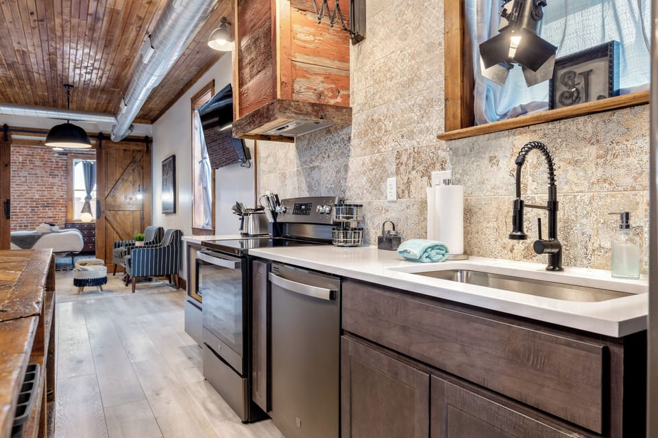 The kitchen work area features a deep sink, dishwasher, electric range, patterned backsplash, and long counter.