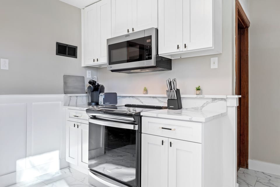Kitchen cooking wall with white cabinetry, stainless electric range, over-the-range microwave, coffee maker, toaster and knife block.