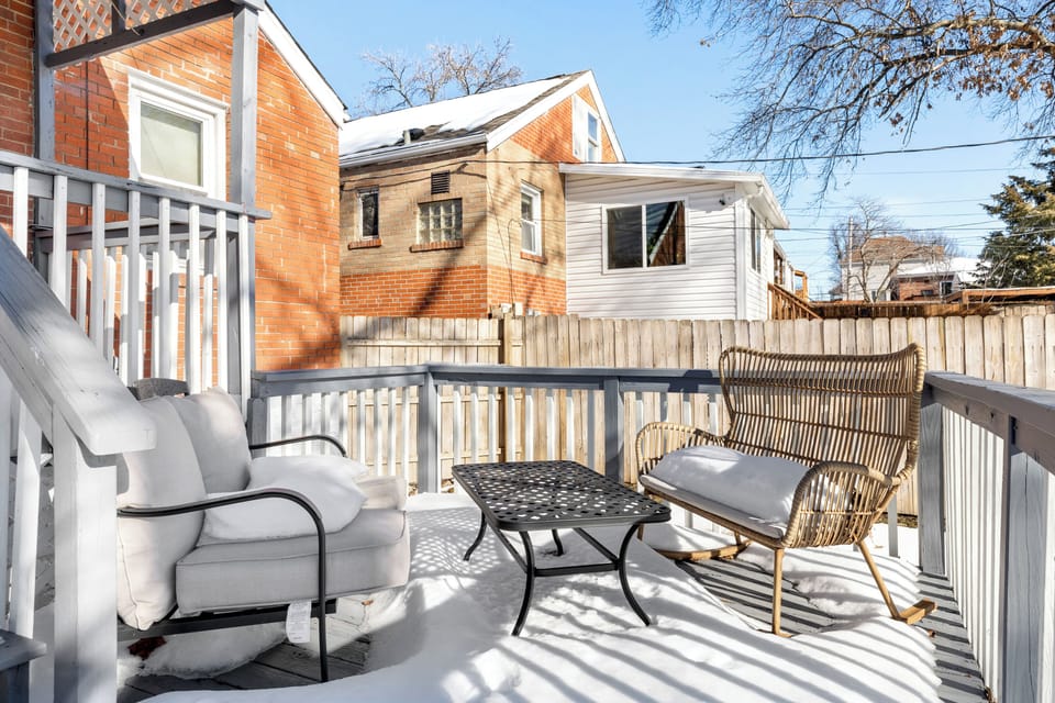 Winter view of the rear deck with outdoor chairs, a low table, railing, and a fenced yard beyond.