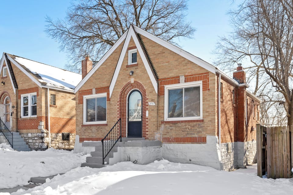 Angled winter view of the brick home with its arched front entrance, 6718 address plaque, front steps, and side gate.