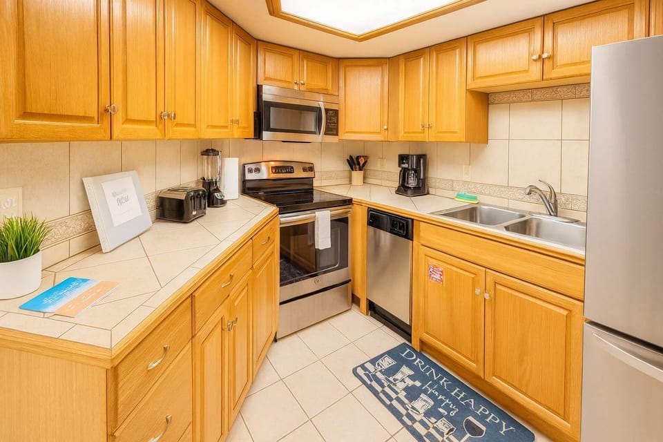 Modern kitchen with stainless steel appliances, oak cabinetry, tiled counters, and double sink. Includes coffee maker, toaster, blender, and welcome binder. Bright, clean, and fully equipped—perfect for extended stays or weekend getaways.