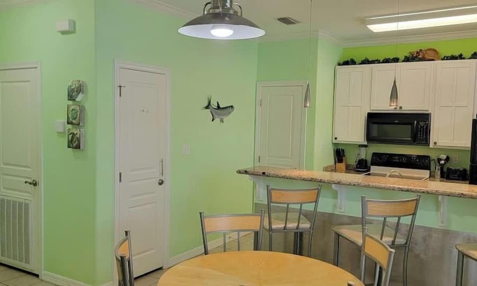 Enjoy meals in this bright kitchen and dining space featuring a round table, breakfast bar with stools, white cabinets, and modern appliances. Clean décor and natural light create a welcoming hub for cooking, dining, and gathering.