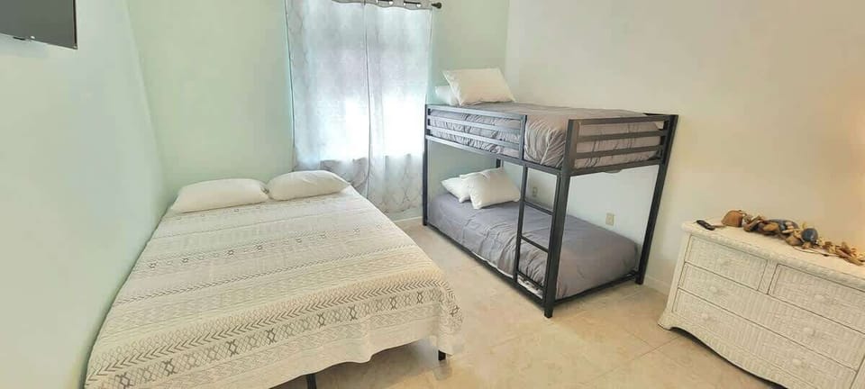 Bright, efficient bedroom featuring a double bed, sturdy bunk bed, soft natural light, and a wall‑mounted TV. A practical, comfortable setup ideal for families or groups needing flexible sleeping space and an easy, restful stay.