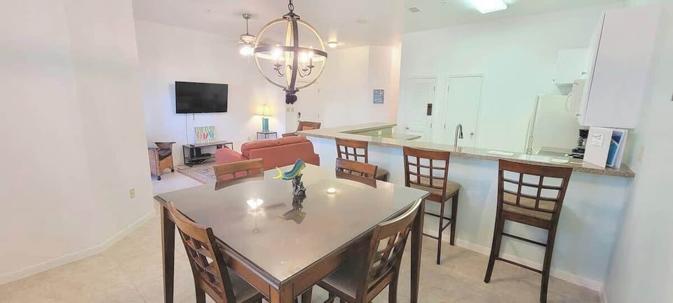 Bright open‑concept living, dining, and kitchen space featuring a modern chandelier, cozy seating, and a sleek breakfast bar. Perfect for gathering, relaxing, and enjoying effortless flow throughout this inviting coastal‑inspired layout.