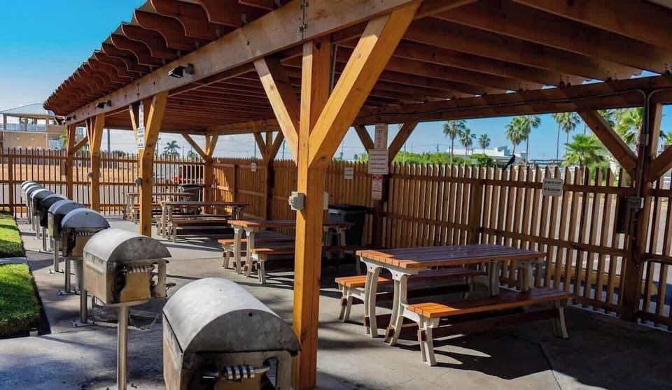 Spacious outdoor BBQ area featuring multiple grills, shaded picnic tables, and a clean, well‑kept setting surrounded by palms. A convenient communal space perfect for cookouts, gatherings, and enjoying warm coastal days with family and friends.