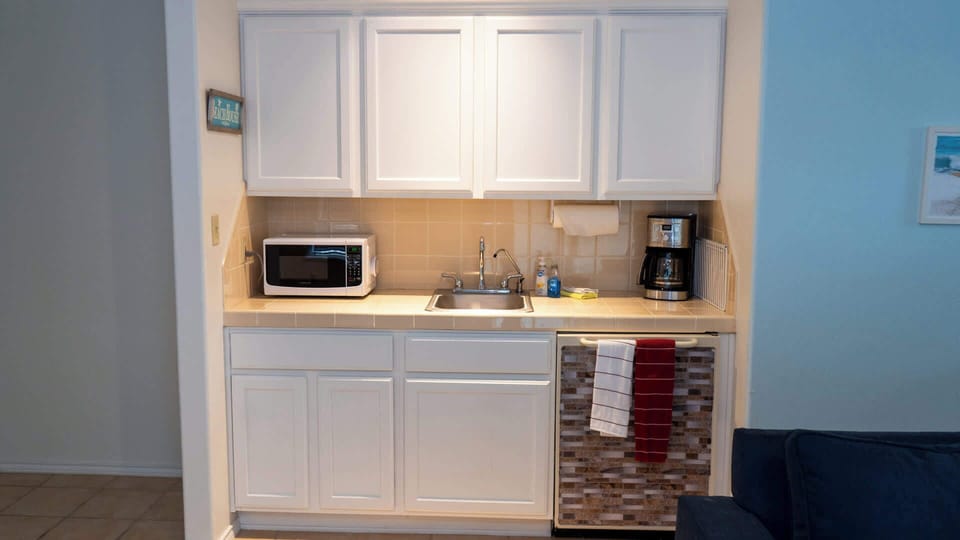 Handy kitchenette with white cabinetry, microwave, sink, and coffee maker—perfect for quick snacks or morning brews. Enjoy practical convenience and coastal charm for guests seeking comfort and ease during their beach stay.