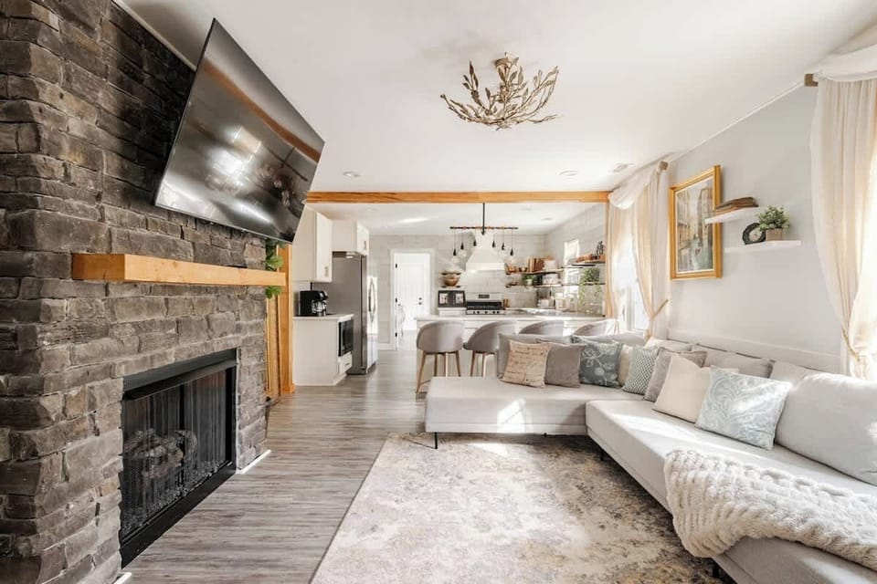 Bright, open-concept living room with a cozy stone fireplace, Smart TV, and plush sectional. A warm gathering space for movie nights, relaxing after the sauna, or spending time together during your Charlotte stay.