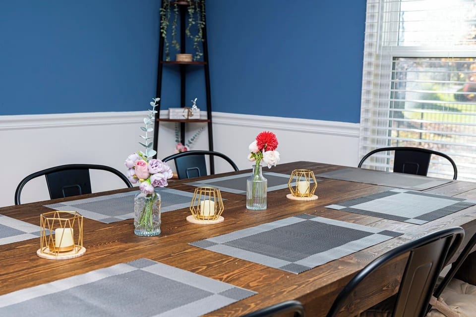 A rustic dining table, adorned with gray placemats, colorful flowers, and golden candles, invites you to a warm and cozy meal against a calming blue wall.