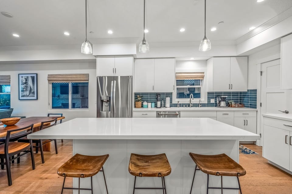 Bright and airy completely stocked chef's kitchen features white quartz countertops, a blue tile backsplash, walk in pantry, and spacious cabinetry. All kitchen supplies are brand new so you can whip up anything from a quick bite to a gourmet meal.