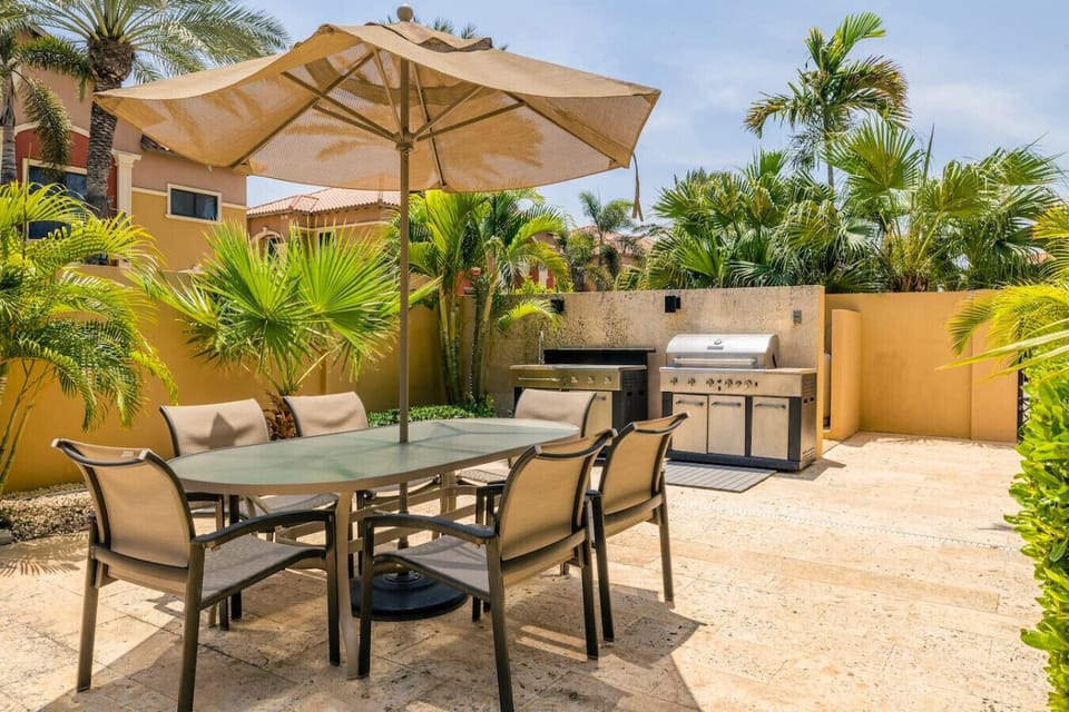 Sunny outdoor dining area with a stylish table, umbrella, and a BBQ grill for al fresco meals.