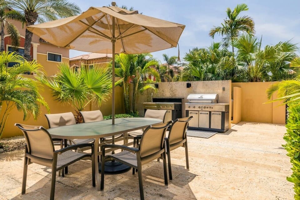 Sunny outdoor dining area with a stylish table, umbrella, and a BBQ grill for al fresco meals.