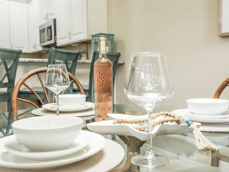 Glass dining table set with white dishes and a bottle of rosé wine in a cozy kitchen setting