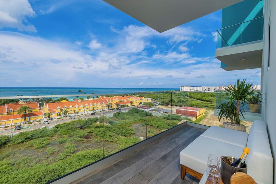 Modern balcony overlooking turquoise Caribbean waters, bright rooftops, and lush greenery—complete with stylish seating for enjoying sunset toasts and tropical breezes.