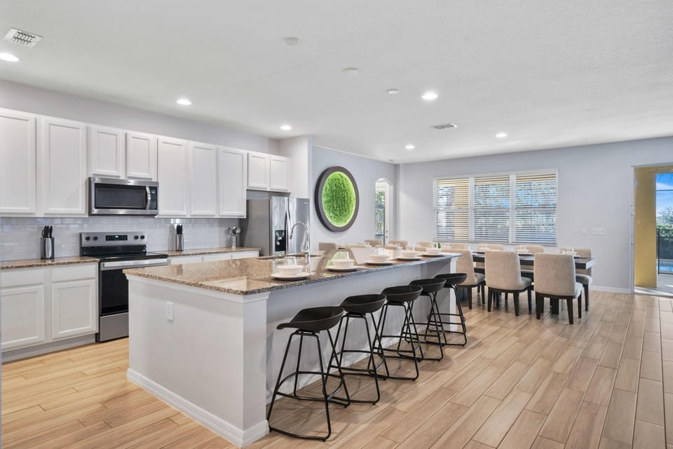- Modern kitchen with granite counters and stainless steel  
- Large island with bar seating and dining table nearby  
- Orlando rental with fully equipped kitchen for families