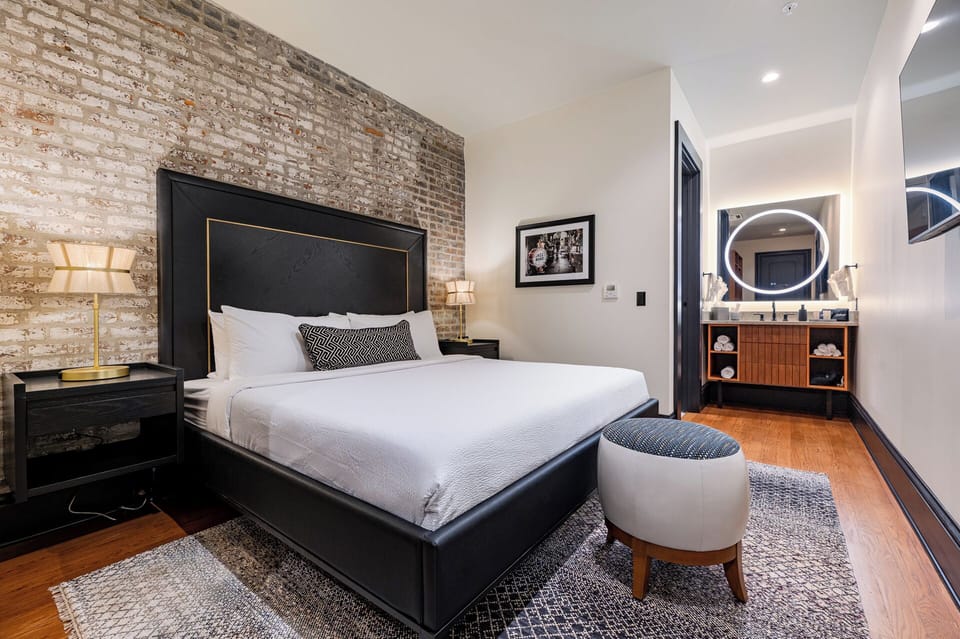 A chic bedroom featuring an exposed brick wall, plush king-sized bed, and flat-screen TV.