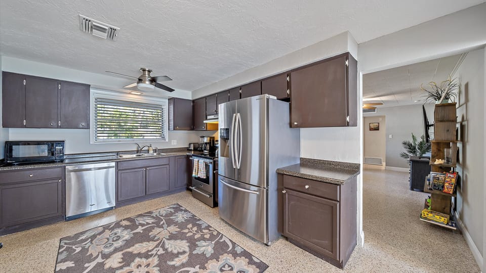 A well-lit kitchen with modern stainless steel appliances, dark cabinets, and a spacious counter.