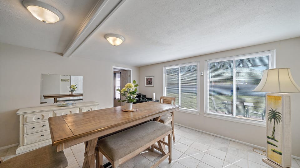 A spacious dining room with a long wooden table, bench seating, a large dresser, and windows overlooking the yard.