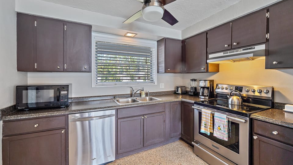 A kitchen with modern stainless steel appliances, dark cabinets, granite countertops, and a window for natural light.