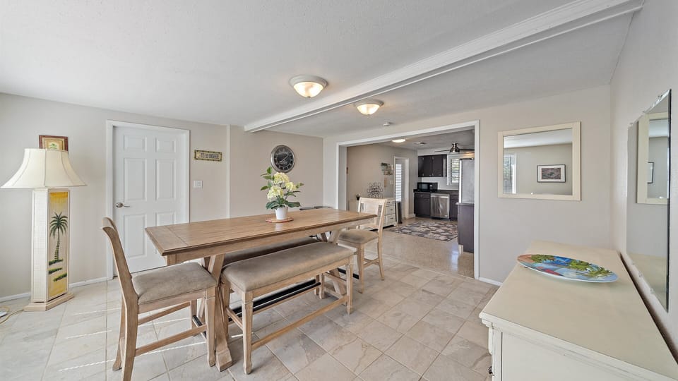 A large dining room with a long wooden table, bench seating, a decorative dresser, and an open layout to the kitchen.