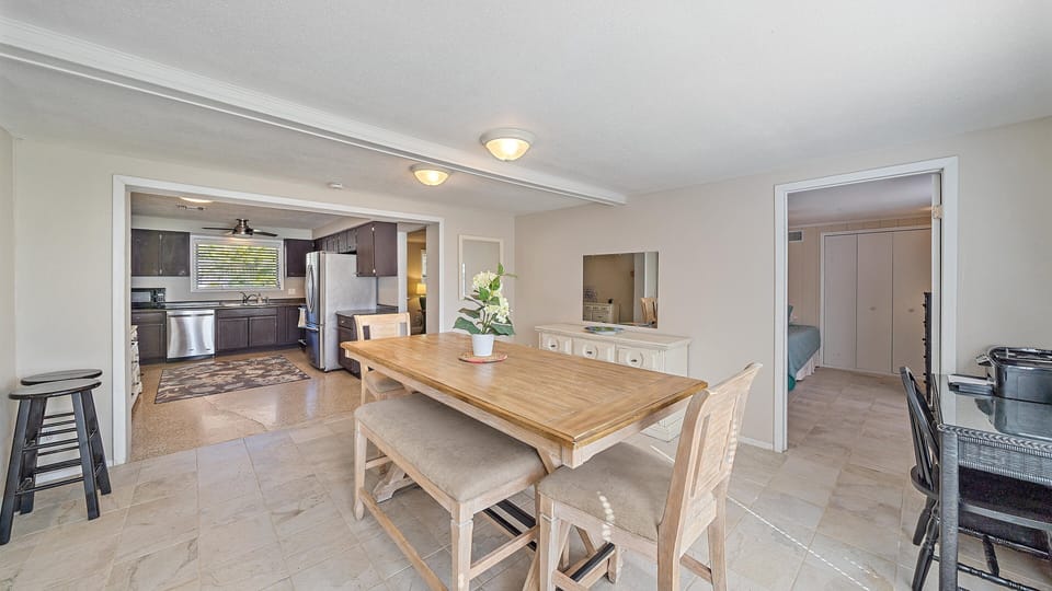 A large dining area with a wooden table and bench, a white dresser, and an open layout connecting to the kitchen.