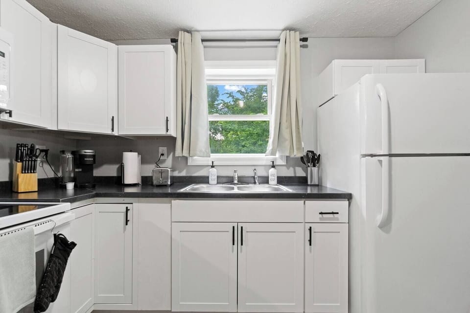 Well-equipped kitchen featuring a fridge, toaster, knife set, and coffee maker, with a window offering a lovely view while you cook.