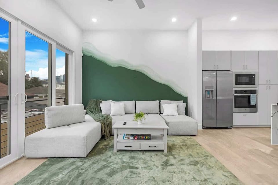 Bright living area w/ comfy seating, green accent wall & large windows that fill the space w/ natural light.