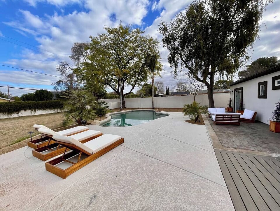 Private pool with reclining chairs, surrounded by a secluded lush yard for relaxation.