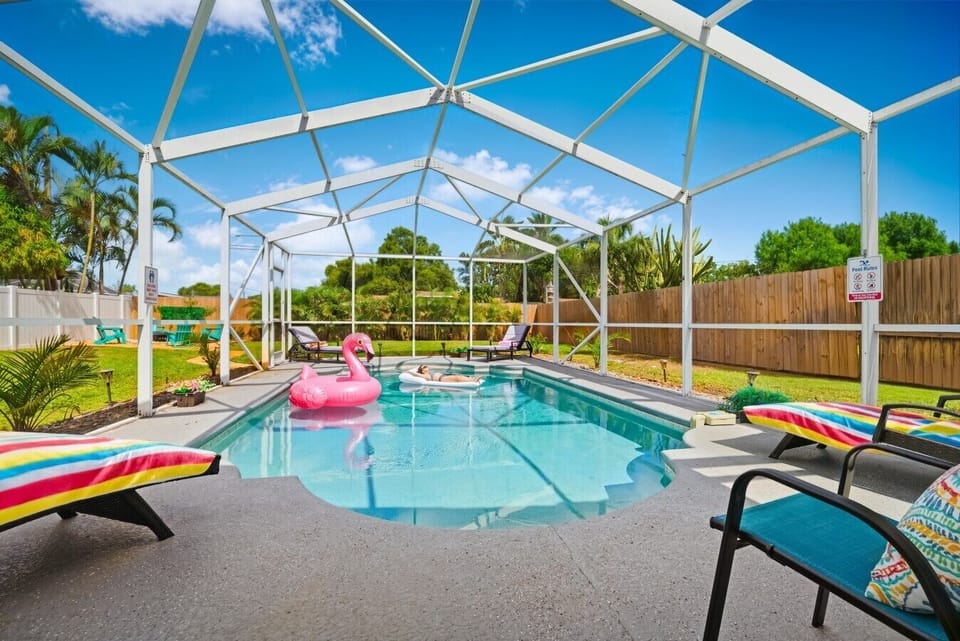 Screened-in private pool at Sun Oasis, a vacation rental in St. Petersburg, FL — crystal-clear water, lounge chairs, and lush tropical landscaping in a fully fenced backyard.