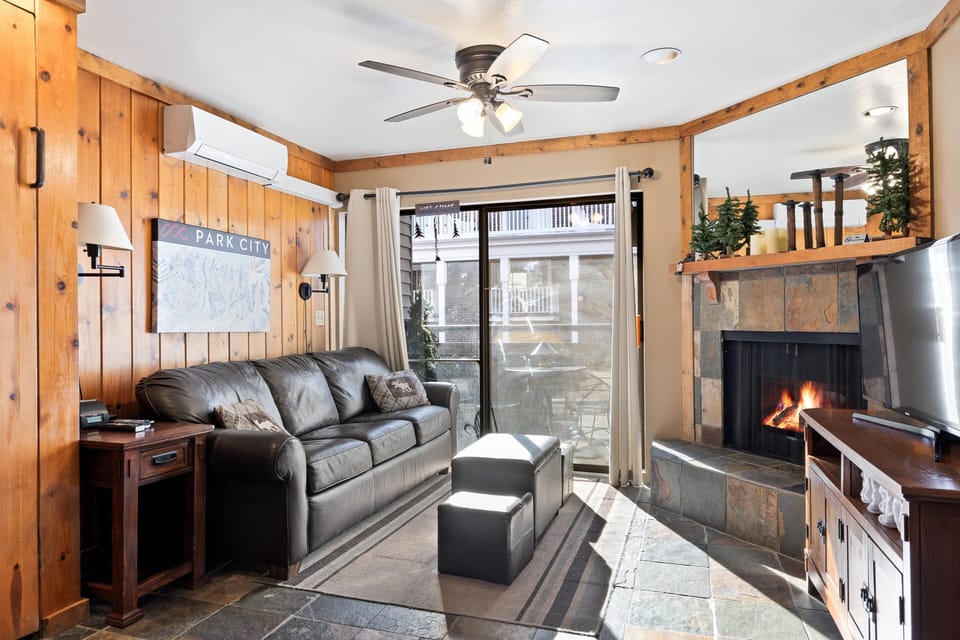 Inviting living room with a stone fireplace, leather sofa, and private patio access—perfect for relaxing after a Park City ski day.