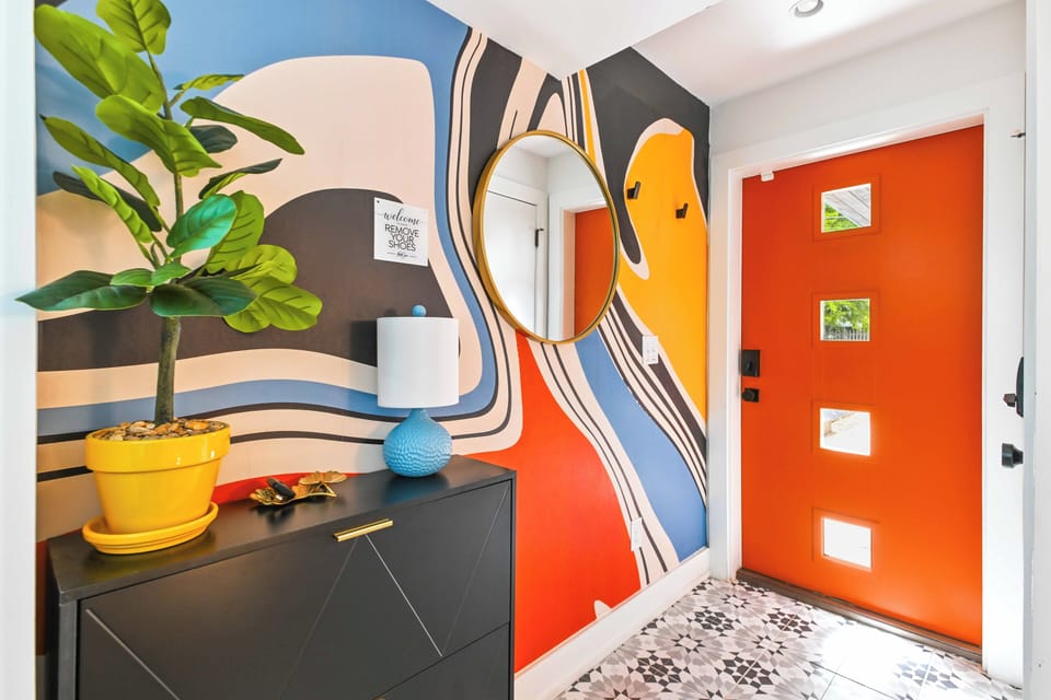Bold and vibrant entryway featuring a statement mural, eye-catching orange door, and stylish decor creating a fun and unforgettable first impression.
