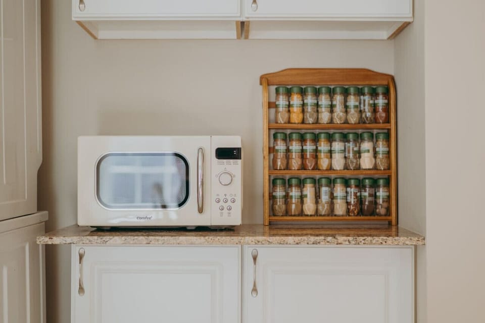 Countertop with a microwave oven next to a wooden spice rack filled with various spice jars