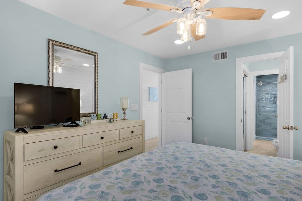 Rest in this tranquil bedroom with soft coastal colors, ceiling fan, and convenient TV setup for your evening relaxation.