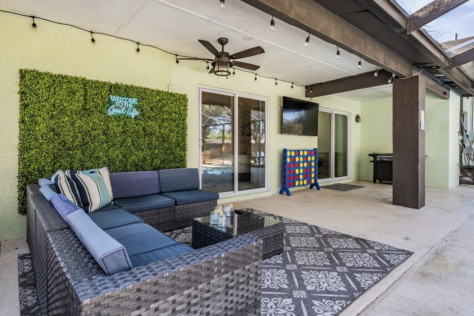 Lounge in the cozy outdoor lanai with comfy seating, a glowing “Welcome to the Good Life” sign, twinkling string lights, and giant Connect Four, perfect for relaxed socializing, gaming, or just unwinding after a long day.