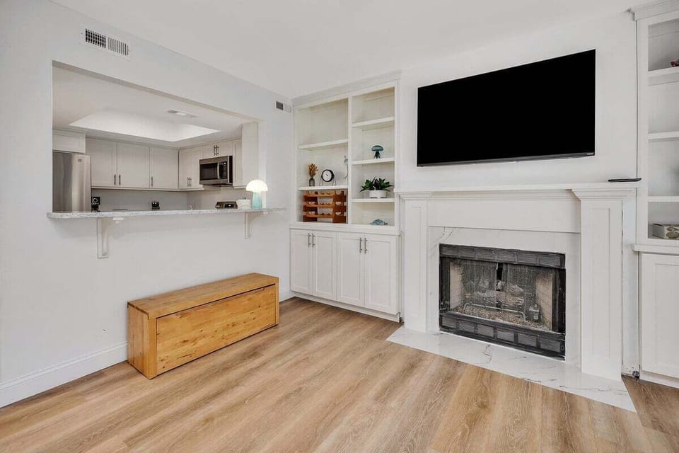 Living room with TV, fireplace, built-ins, and shutters