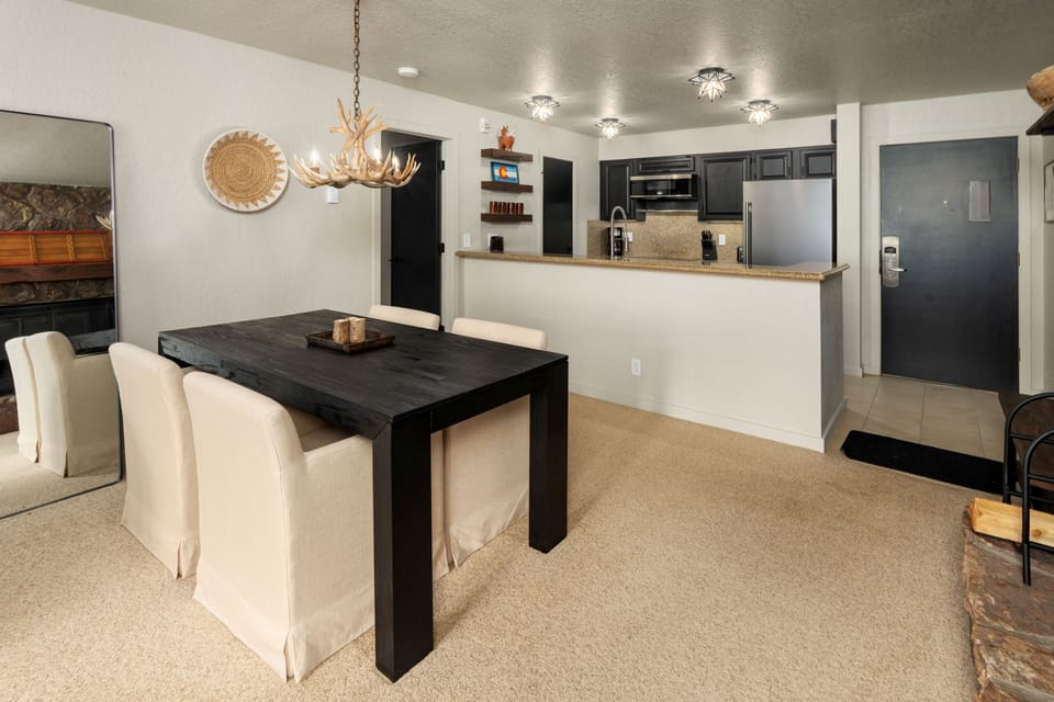 Gather around the elegant dining table for meals, with the fully equipped kitchen right at your fingertips. The rustic chandelier and cozy fireplace create a warm, inviting atmosphere for memorable evenings.