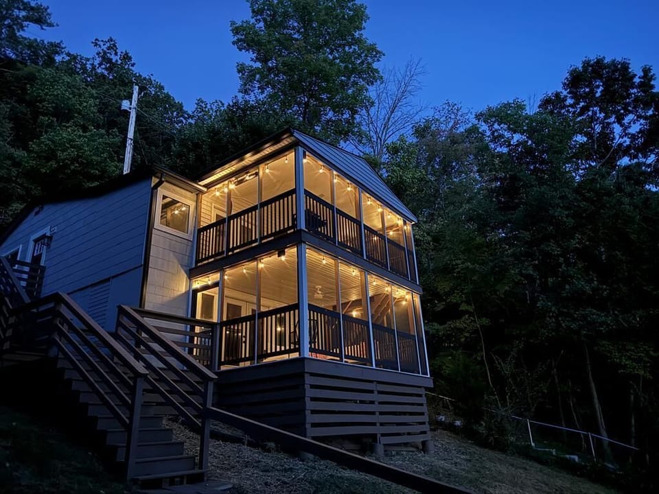 Charming two-story house with glowing string-lit porches, nestled in nature.