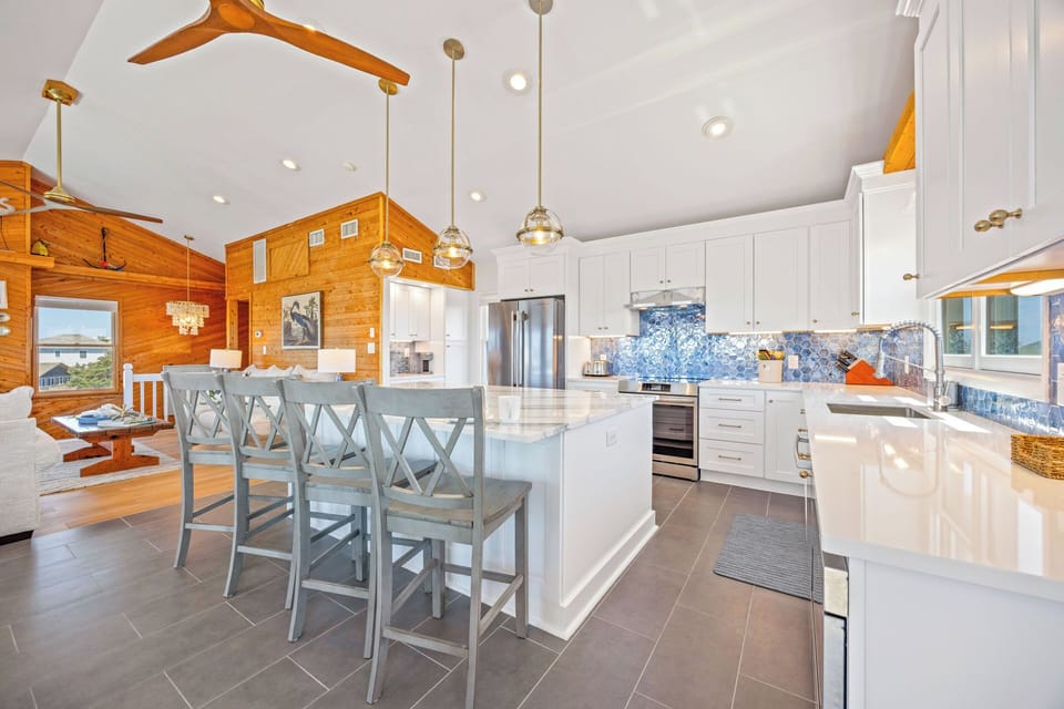 Picture yourself preparing meals in this airy, light-filled kitchen featuring a spacious island with seating for four. Gleaming white cabinetry, stainless appliances, and stunning blue tile backsplash create a cheerful coastal vibe perfect for your getaway