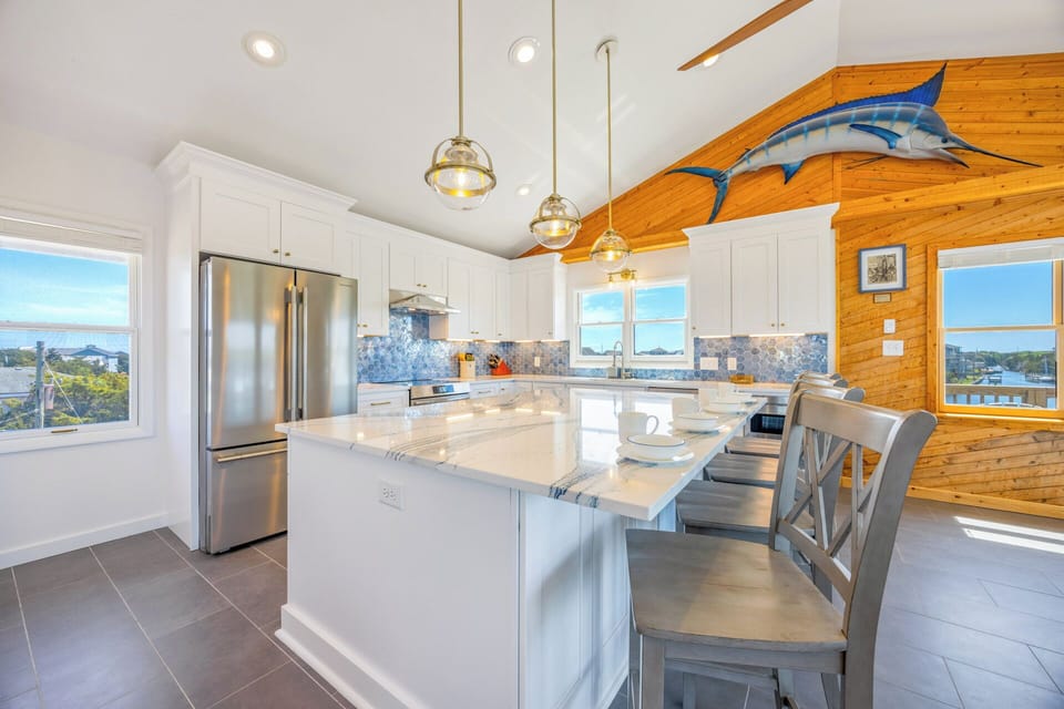 Cook up your vacation favorites in this bright, open kitchen with marble countertops, stainless steel appliances, and coastal-inspired touches like the marlin sculpture overhead.