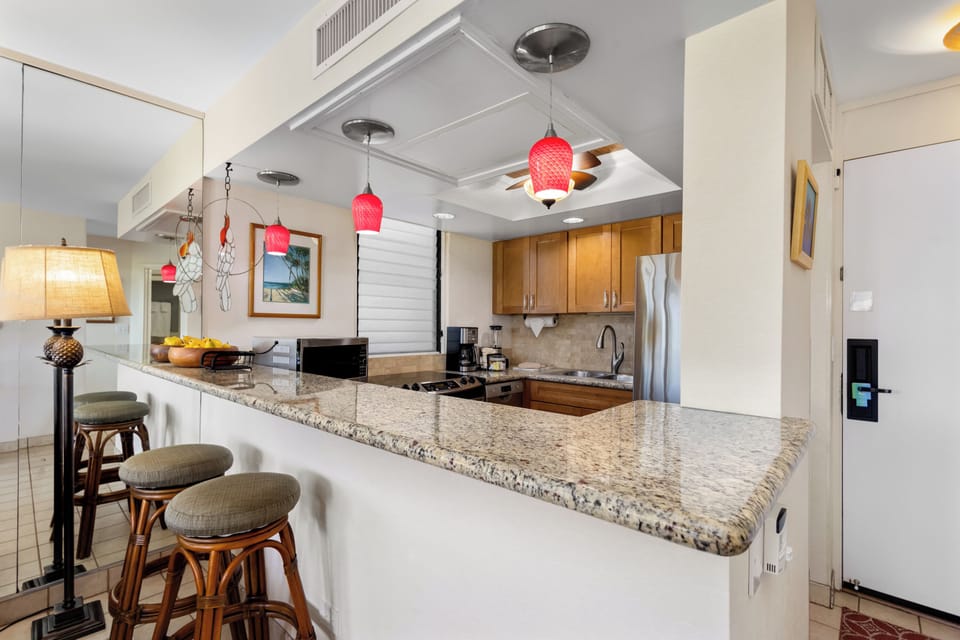 Your fully equipped kitchen features granite countertops, warm wood cabinetry, and cheerful pendant lighting. Gather at the breakfast bar with comfortable seating—perfect for morning coffee or casual meals together.