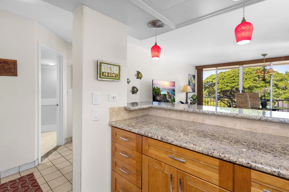 Cook your favorite meals at this granite-topped kitchen island, with lush green views and cheerful pendant lights above. A well-equipped space awaits your culinary adventures.