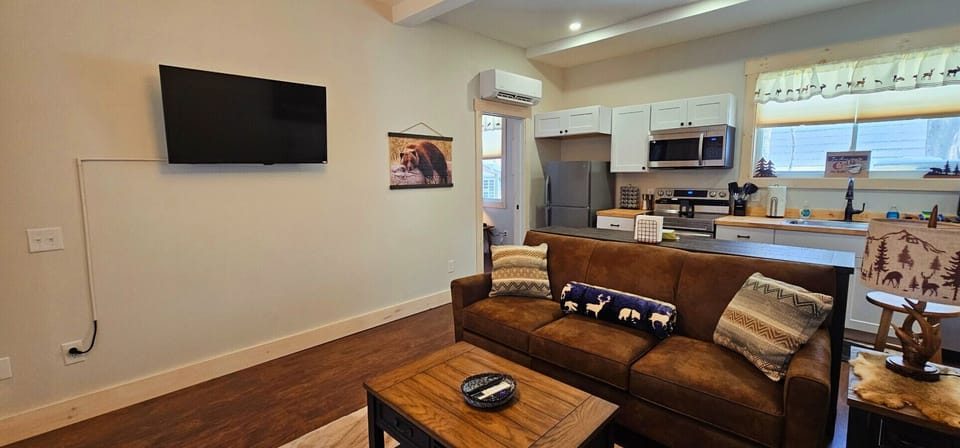 Comfortable living room with a smart TV, cozy leather sofa, rustic cabin décor, and an open layout connecting seamlessly to the fully equipped kitchen.