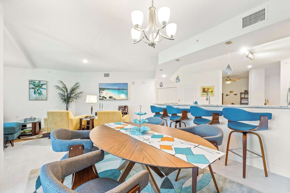 Open-concept living and dining area with modern furnishings and a breakfast bar with blue stools.
