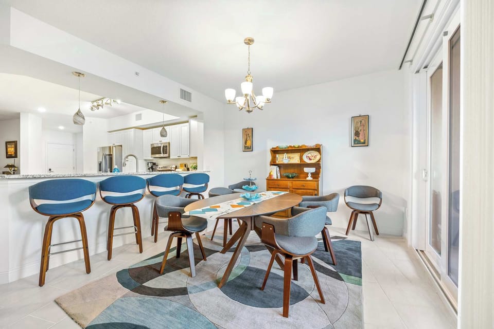 Modern dining area with a wooden table, blue and gray chairs, and a kitchen bar with stools.