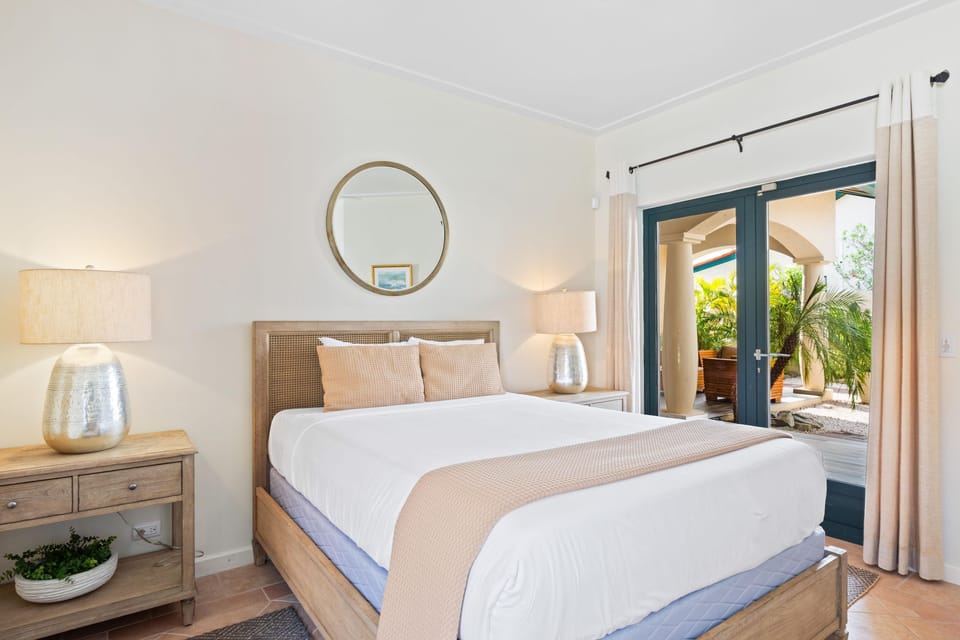 A cozy bedroom with soft lighting and elegant design, offering a serene ambiance enhanced by natural light and a view of the outdoor patio.