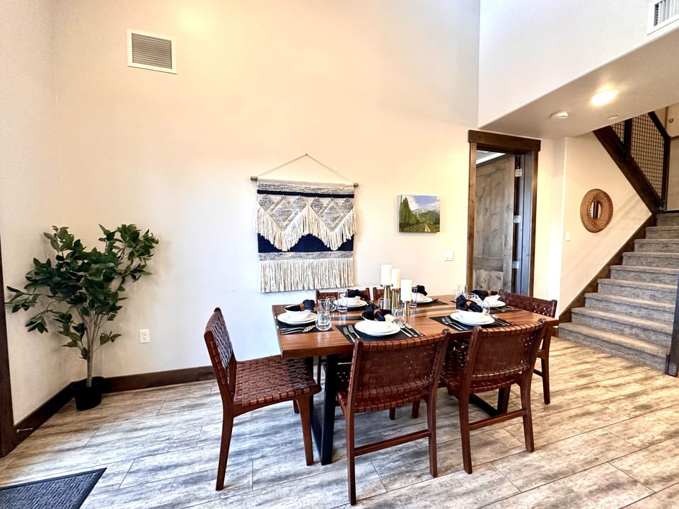 Gather in this stylish dining area featuring a warm wood table and bohemian-inspired woven chairs. The space is bright and airy with high ceilings and a chic tapestry accent, perfect for group meals.