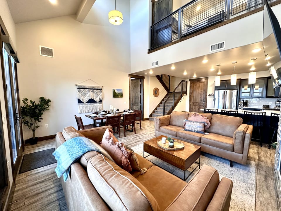 Relax in this luxurious open-concept living area. It features a stunning floor-to-ceiling stone fireplace, plush leather seating, and a modern kitchen with high-end finishes, perfect for mountain getaways.