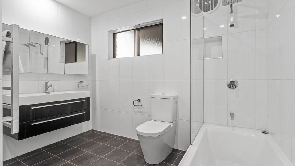 Sleek, modern bathroom featuring a rainfall shower, deep soaking tub, and pristine, contemporary design.